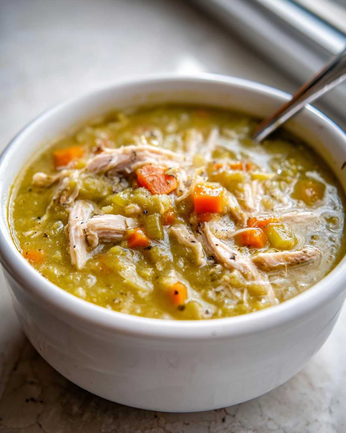 A close-up of a white bowl filled with thick Instant Pot Split Pea Soup with Smoked Turkey, carrots, and celery.
