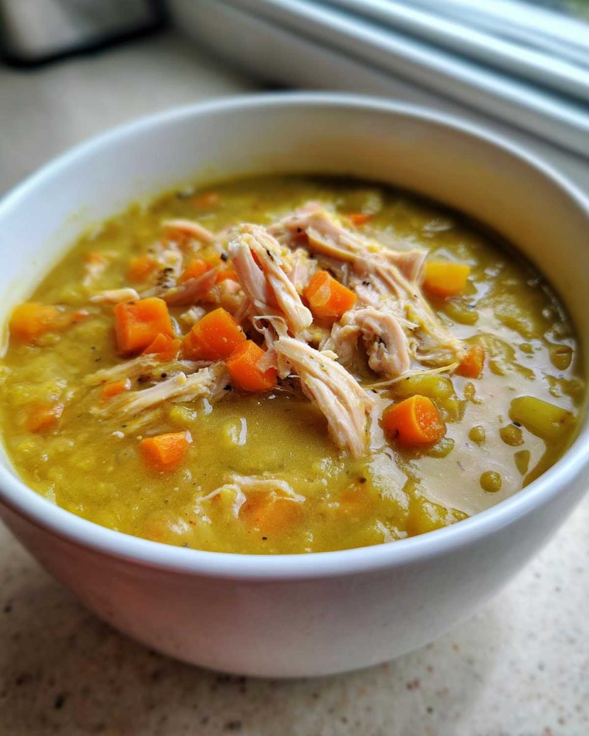 Close-up of a white bowl filled with thick Instant Pot Split Pea Soup with Smoked Turkey, topped with shredded meat and diced carrots.