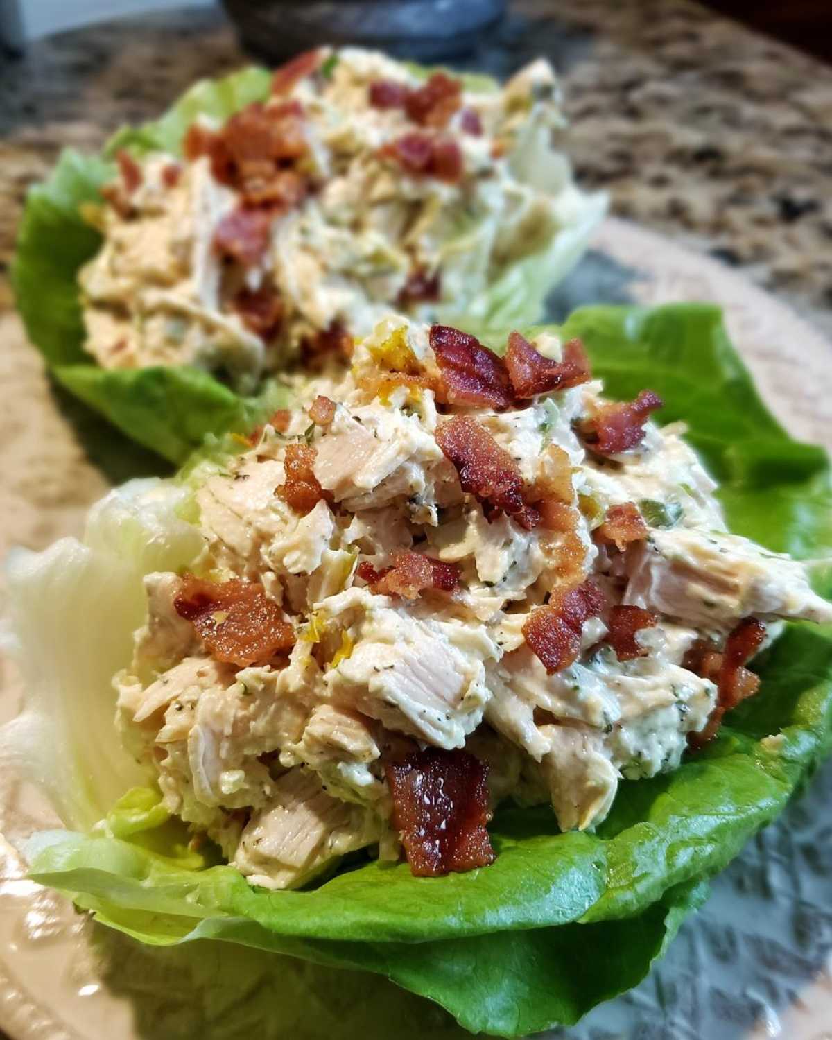 Two servings of Keto Bacon Ranch Chicken Salad Lettuce Boats topped with crispy bacon pieces.