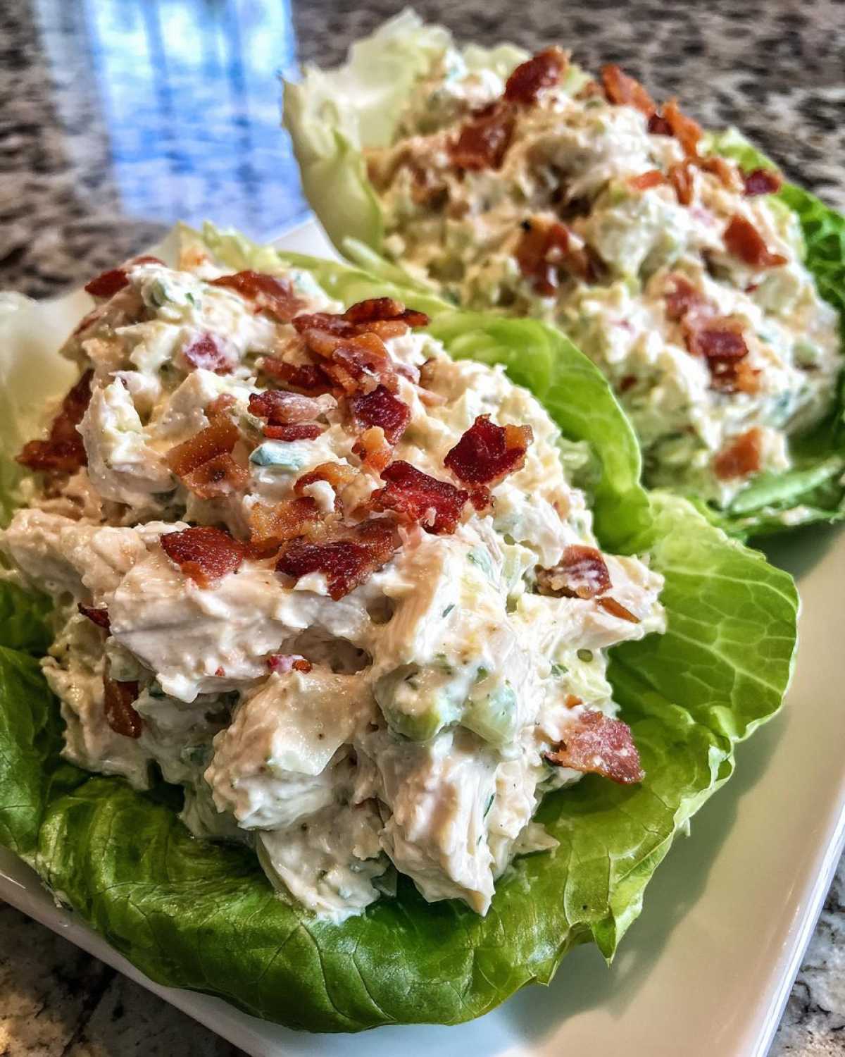Two servings of Keto Bacon Ranch Chicken Salad Lettuce Boats piled high with creamy chicken salad and topped with crispy bacon bits.