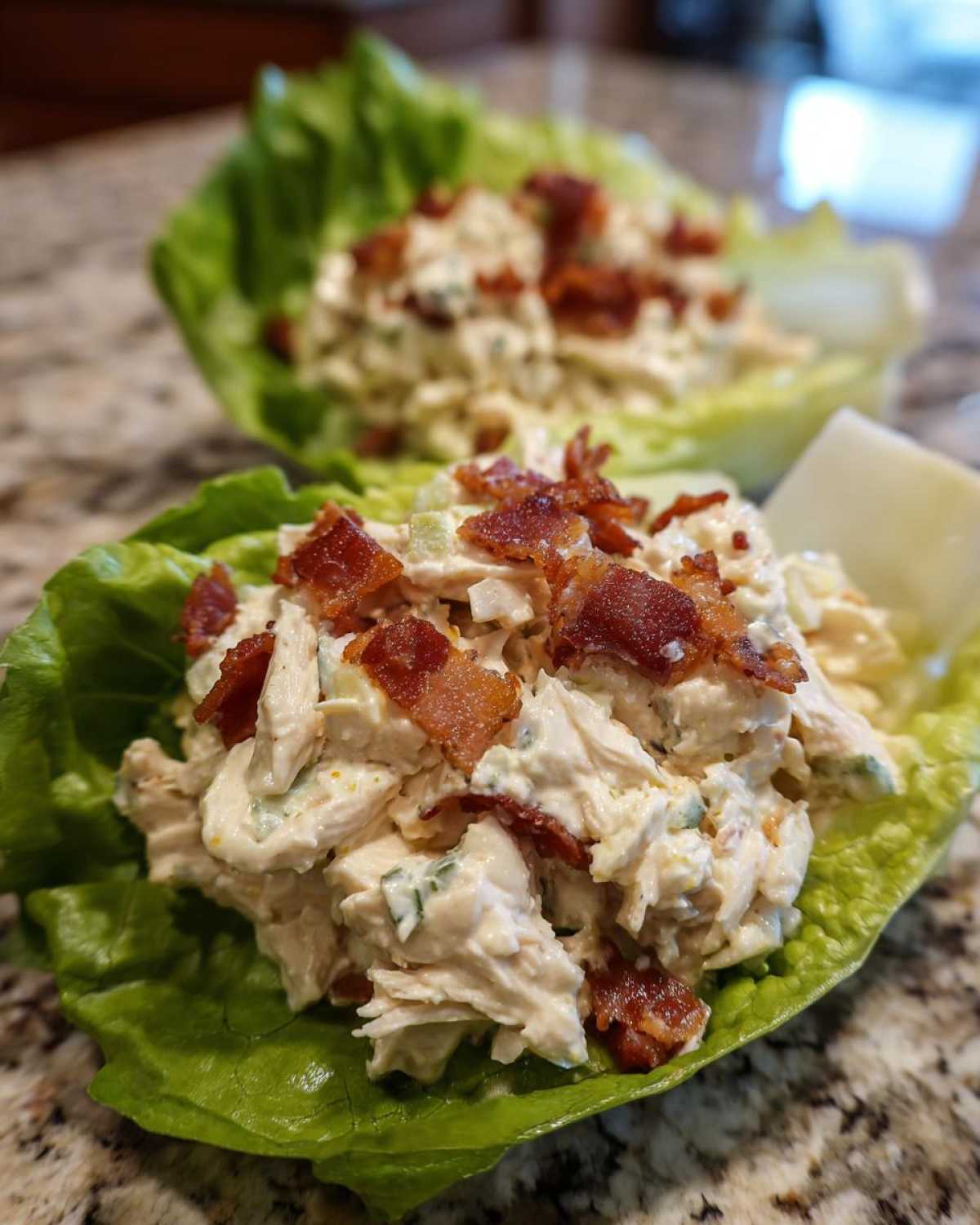 Two servings of Keto Bacon Ranch Chicken Salad Lettuce Boats topped with crispy bacon pieces.