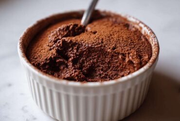 A rich, dark chocolate mousse, dusted with cocoa powder, served in a white ramekin, ready to eat.