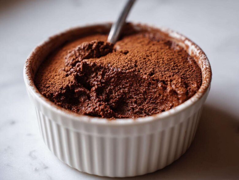 A rich, dark chocolate mousse, dusted with cocoa powder, served in a white ramekin, ready to eat.