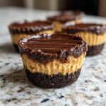 A single, perfectly layered No-Bake Chocolate Peanut Butter Cheesecake Cup in the foreground.