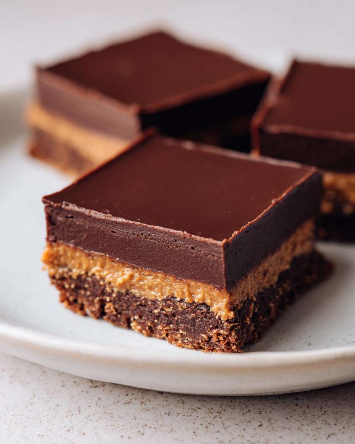 Close-up of a layered No-Bake Espresso Chocolate Fudge Squares bar on a speckled white plate.