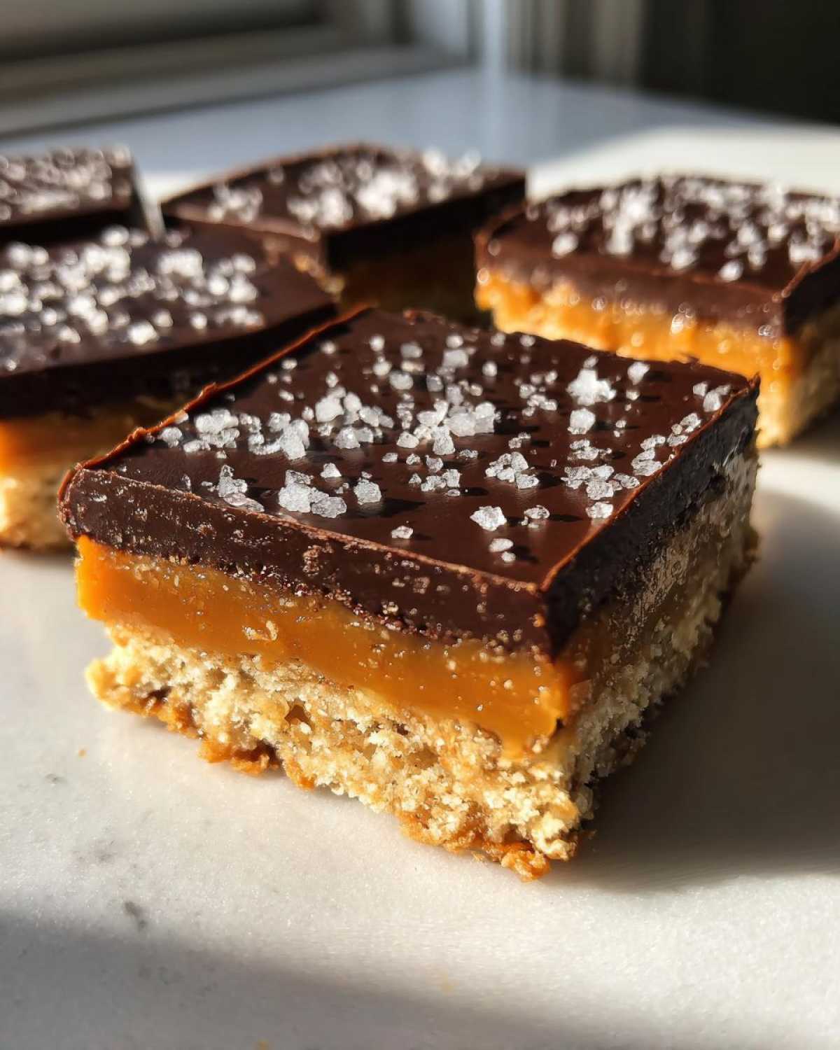 A close-up of a square No-Bake Salted Caramel Pretzel Bar showing the pretzel crust, caramel layer, and chocolate topping with sea salt.