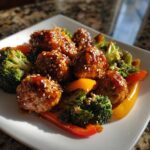 Glazed Sheet Pan Ginger Sesame Chicken Meatballs served with bright green broccoli and colorful bell peppers.