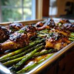 Close-up of glossy Sheet Pan Honey Balsamic Chicken with Asparagus on a metal baking sheet.