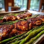 Close-up of glazed Sheet Pan Honey Balsamic Chicken with Asparagus roasting on a metal baking sheet.