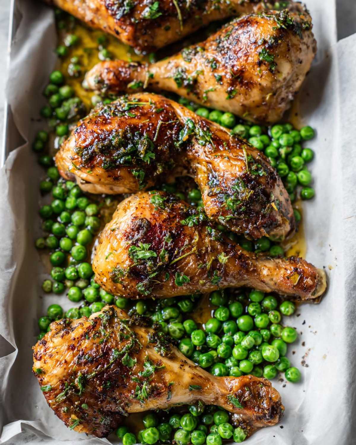 Four golden brown Sheet Pan Lemon Garlic Butter Chicken Legs resting on a bed of bright green peas.