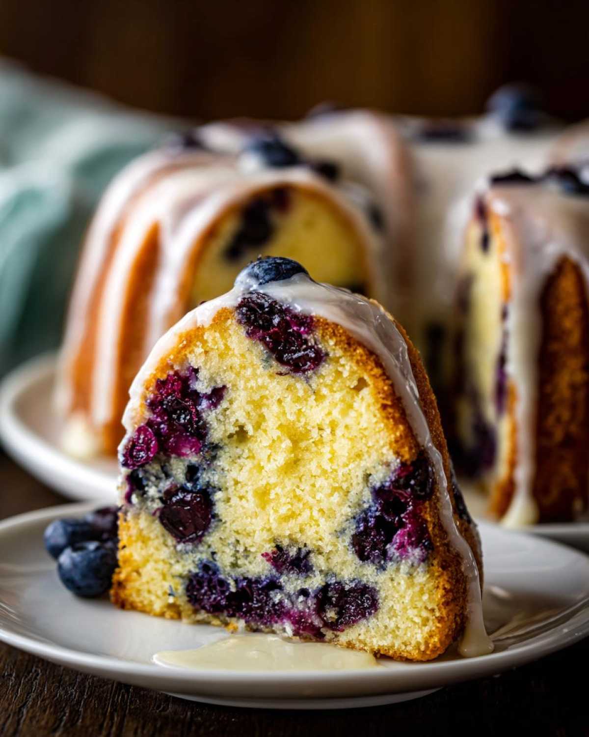 Close-up of a slice of moist Gluten-Free Lemon Blueberry Bundt Cake topped with lemon glaze and fresh blueberries.