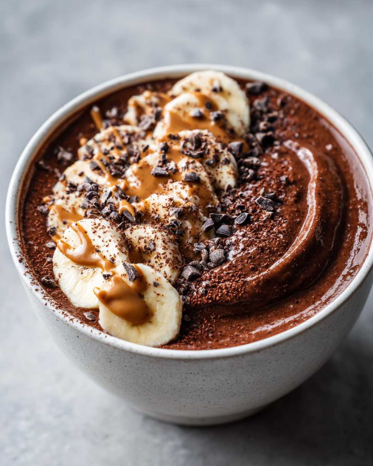 Close-up of a thick Vegan Chocolate Peanut Butter Banana Smoothie Bowl topped with banana slices and cacao nibs.