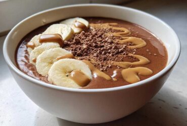 A thick Vegan Chocolate Peanut Butter Banana Smoothie Bowl topped with banana slices, peanut butter drizzle, and cocoa powder.