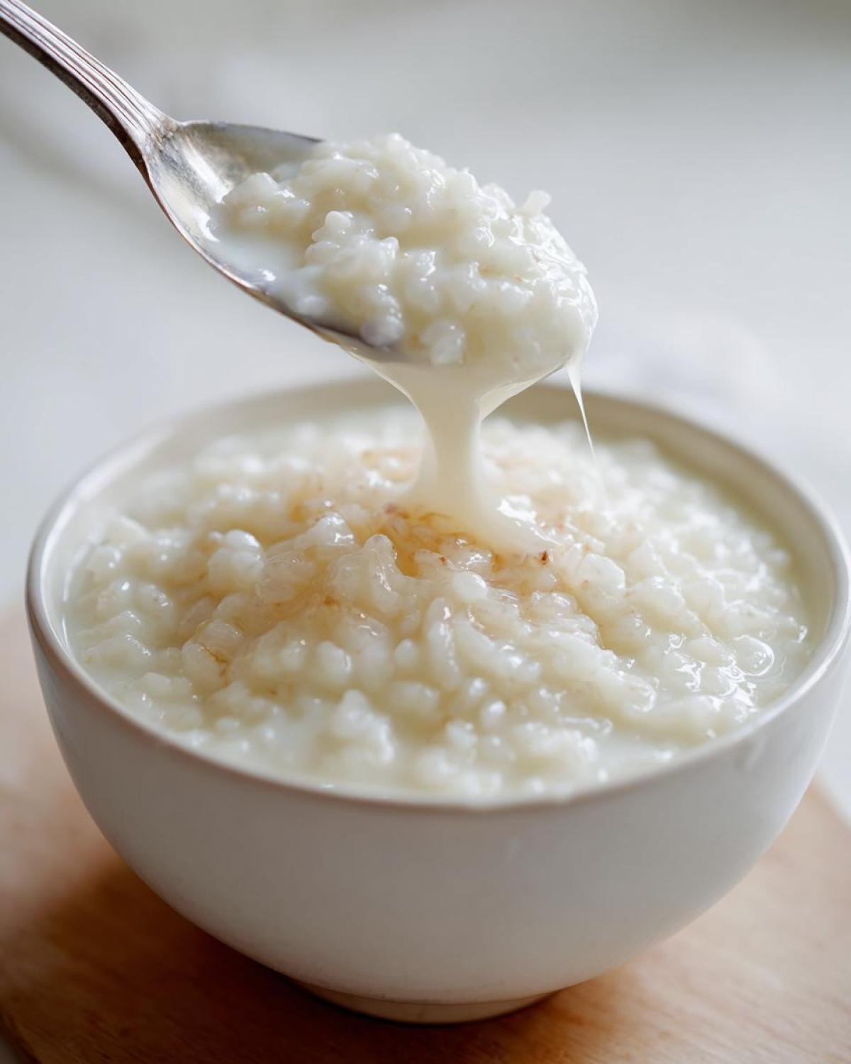 A spoonful of creamy Vegan Creamy Coconut Rice Pudding is lifted from a white bowl, showing its rich texture.