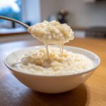 A spoonful of thick, creamy Vegan Creamy Coconut Rice Pudding dripping back into the bowl.