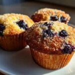 Three golden-brown Vegan Lemon Blueberry Muffins topped with coarse sugar crystals, sitting on a white plate.