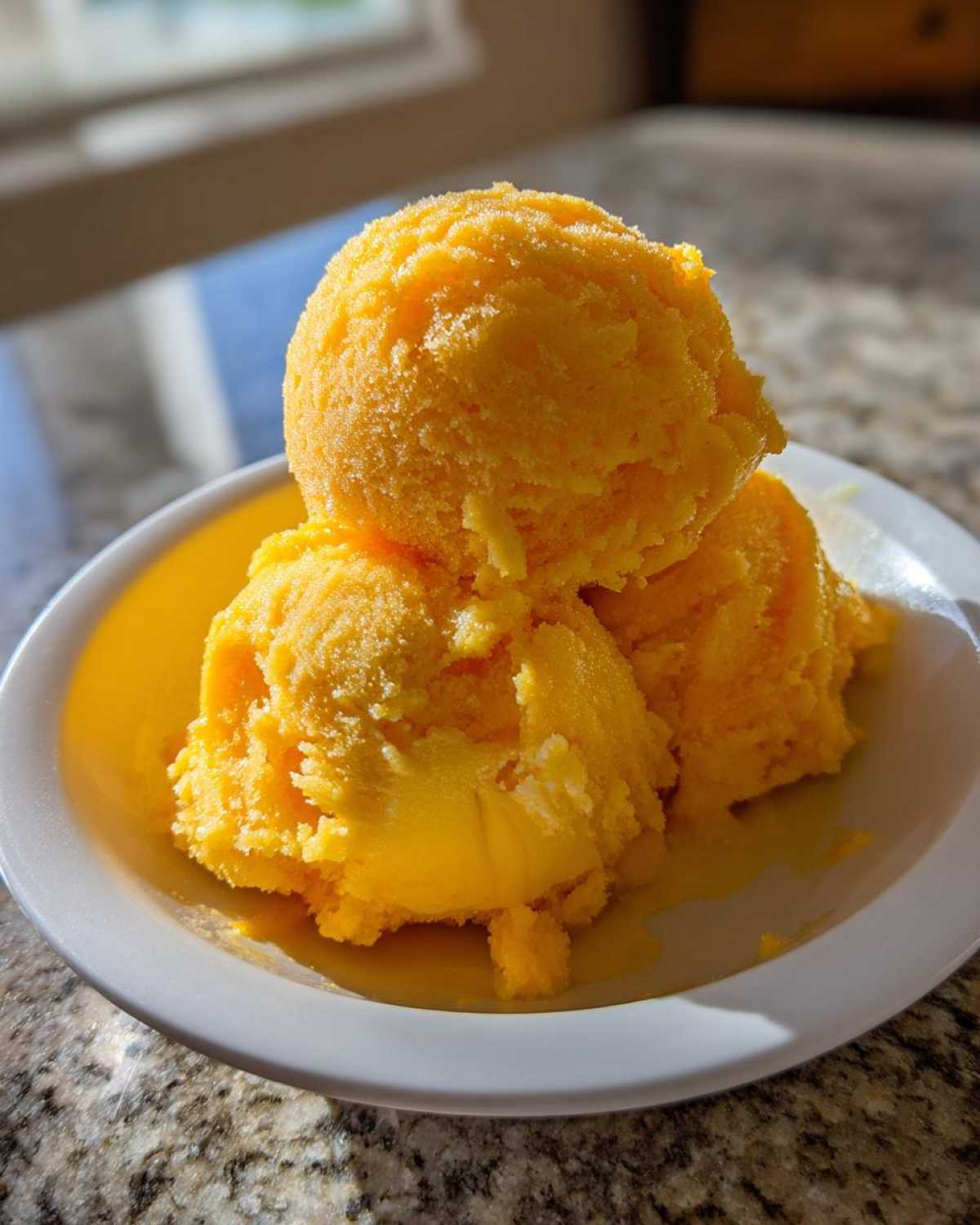 Three bright yellow scoops of Vegan Mango Pineapple Sorbet melting slightly in a white bowl.