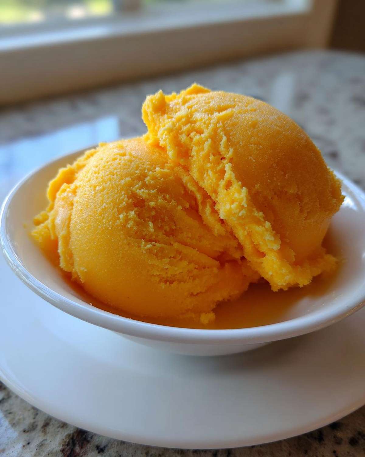 Two bright orange scoops of Vegan Mango Pineapple Sorbet served in a small white bowl.