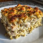 A generous square serving of Cheesy Baked Chicken Alfredo with Crispy Top, showing creamy pasta, chicken pieces, and a golden crust.