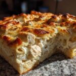 A thick slice of Cheesy Baked Chicken Alfredo with Crispy Top showing creamy pasta, chicken chunks, and a browned, herbed cheese crust.