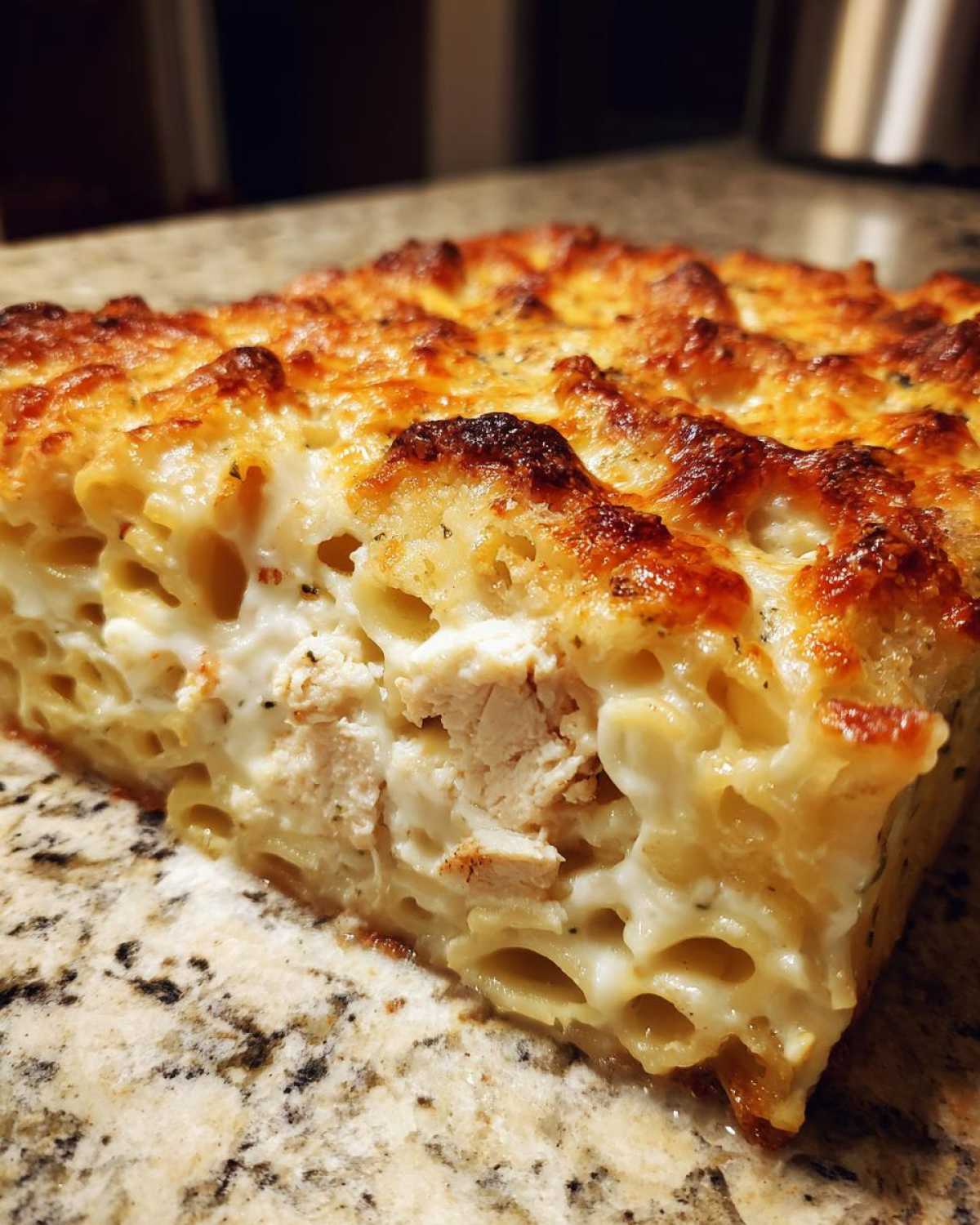 Close-up of a thick slice of Cheesy Baked Chicken Alfredo with crispy, browned cheese topping.