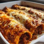 Close-up of baked Cheesy Beef Enchiladas with Rich Sauce, covered in melted, bubbly cheese in a white baking dish.
