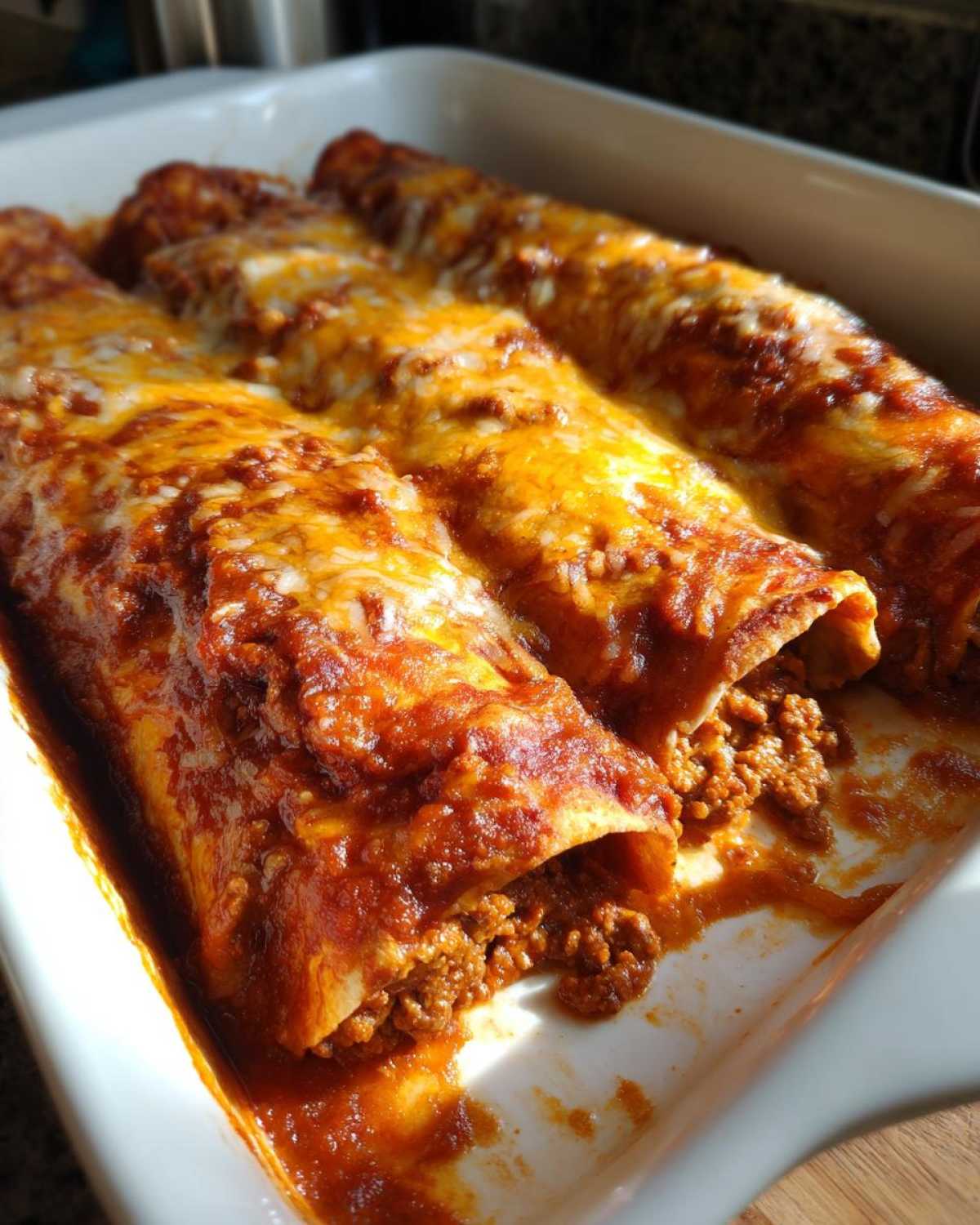 Close-up of freshly baked Cheesy Beef Enchiladas with rich sauce and melted cheese in a white baking dish.