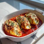 Three baked Cheesy Chicken Alfredo Stuffed Pasta Shells topped with melted cheese and parsley in a rich tomato sauce.