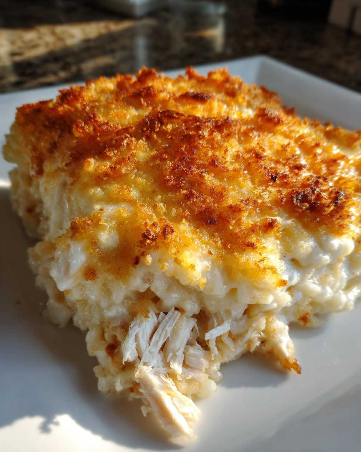 A close-up of a serving of Cheesy Chicken and Rice Bake showing shredded chicken and a crispy golden top.