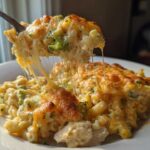 A fork lifts a serving of Cheesy Chicken and Broccoli Pasta Bake, showing dramatic cheese pulls.