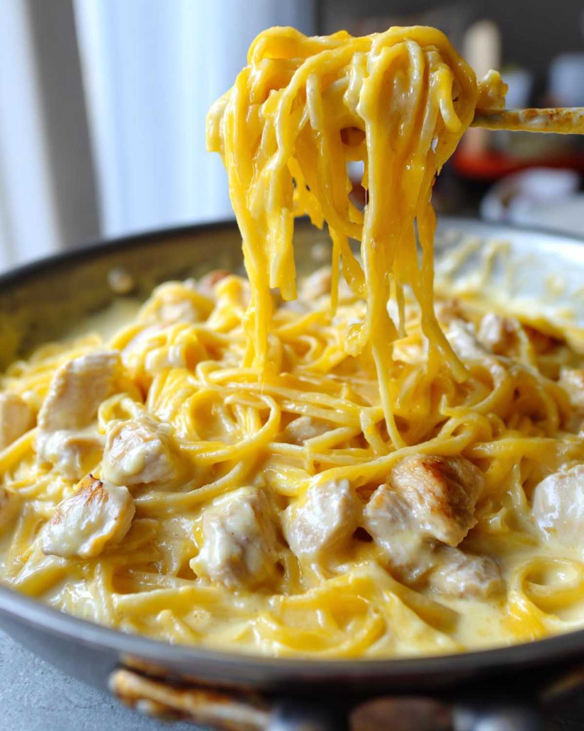 Close-up of long strands of Cheesy Chicken Pasta with Creamy Sauce being lifted from a skillet, showing the thick, rich coating.