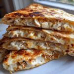 Four stacked, golden-brown slices of Cheesy Chicken Quesadilla with Creamy Filling, oozing melted cheese.