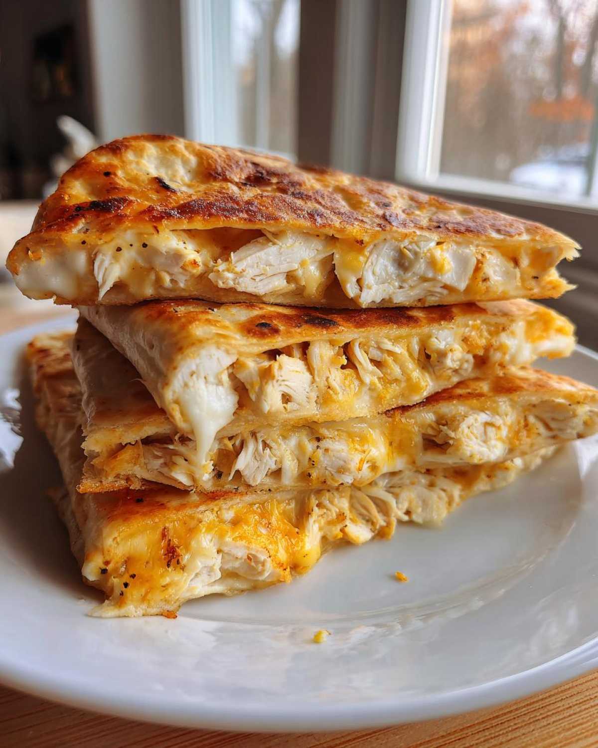 A stack of three golden-brown, cut slices of Cheesy Chicken Quesadilla with Creamy Filling showing melted cheese and shredded chicken.