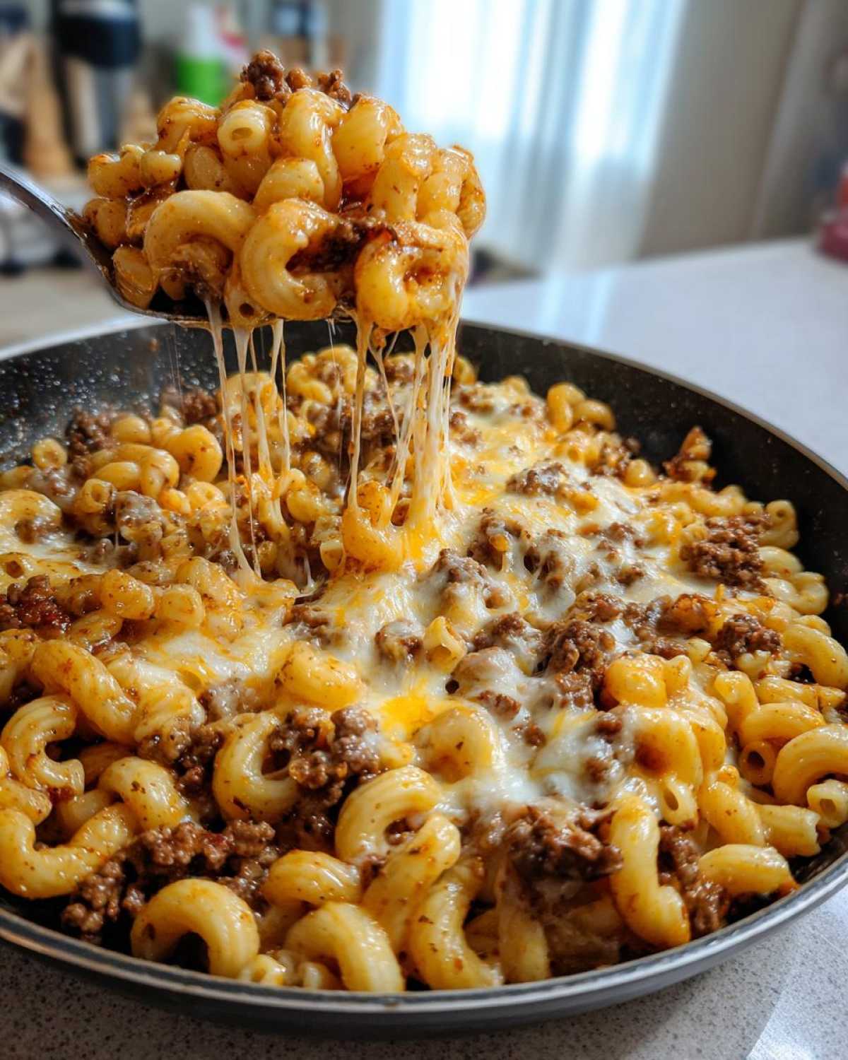 A spoonful of Cheesy Ground Beef Pasta Skillet showing a dramatic cheese pull over the main dish in the pan.