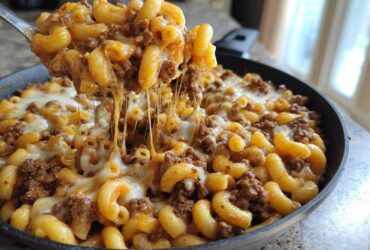 A spoonful of Cheesy Ground Beef Pasta Skillet Comfort Food being lifted, showing long, gooey cheese pulls over the skillet.