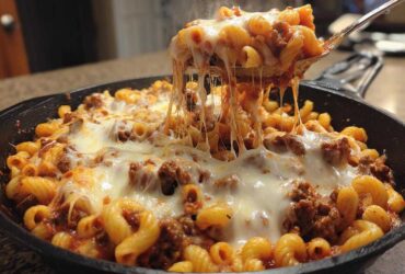 A spoonful of hot Cheesy Ground Beef Pasta Skillet with Mozzarella lifts out of the pan, showing long, melted cheese strings.
