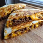 Two halves of a golden-brown Cheesy Ground Beef Quesadilla stacked, showing melted cheese and seasoned ground beef filling.