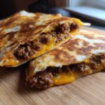 Two halves of a golden-brown Cheesy Ground Beef Quesadilla cut open, showing melted cheddar cheese and seasoned ground beef filling.