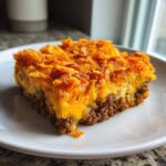 A square serving of Cheesy Ground Beef Queso Bake Comfort Dish with a crunchy topping.