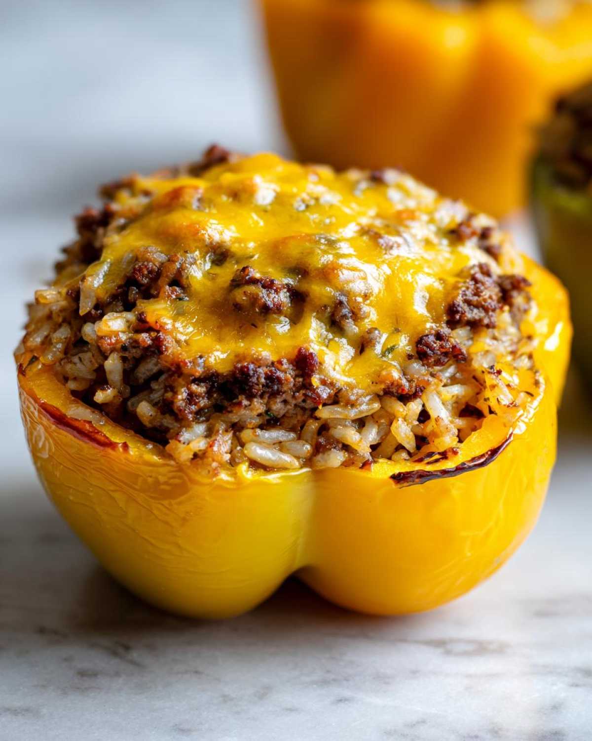 A close-up of a baked yellow bell pepper stuffed with ground beef, rice, and topped with melted cheddar cheese.