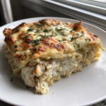 A generous slice of Creamy Alfredo Chicken Bake Easy Comfort Meal with layers of pasta, chicken, and a bubbly, browned cheese topping sprinkled with parsley.