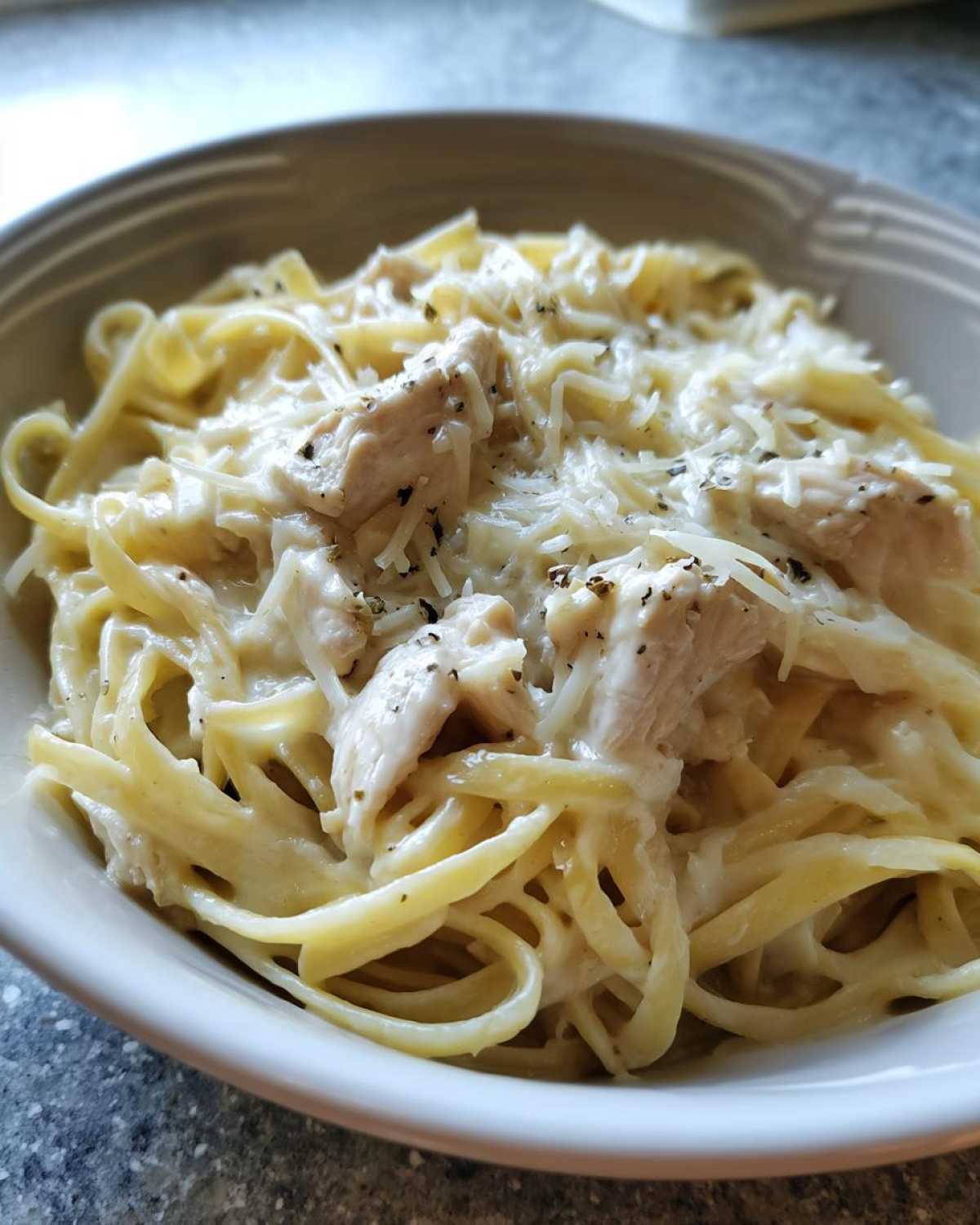 Close-up of a bowl filled with Creamy Alfredo Pasta with Chicken and Cheese, topped with grated Parmesan.