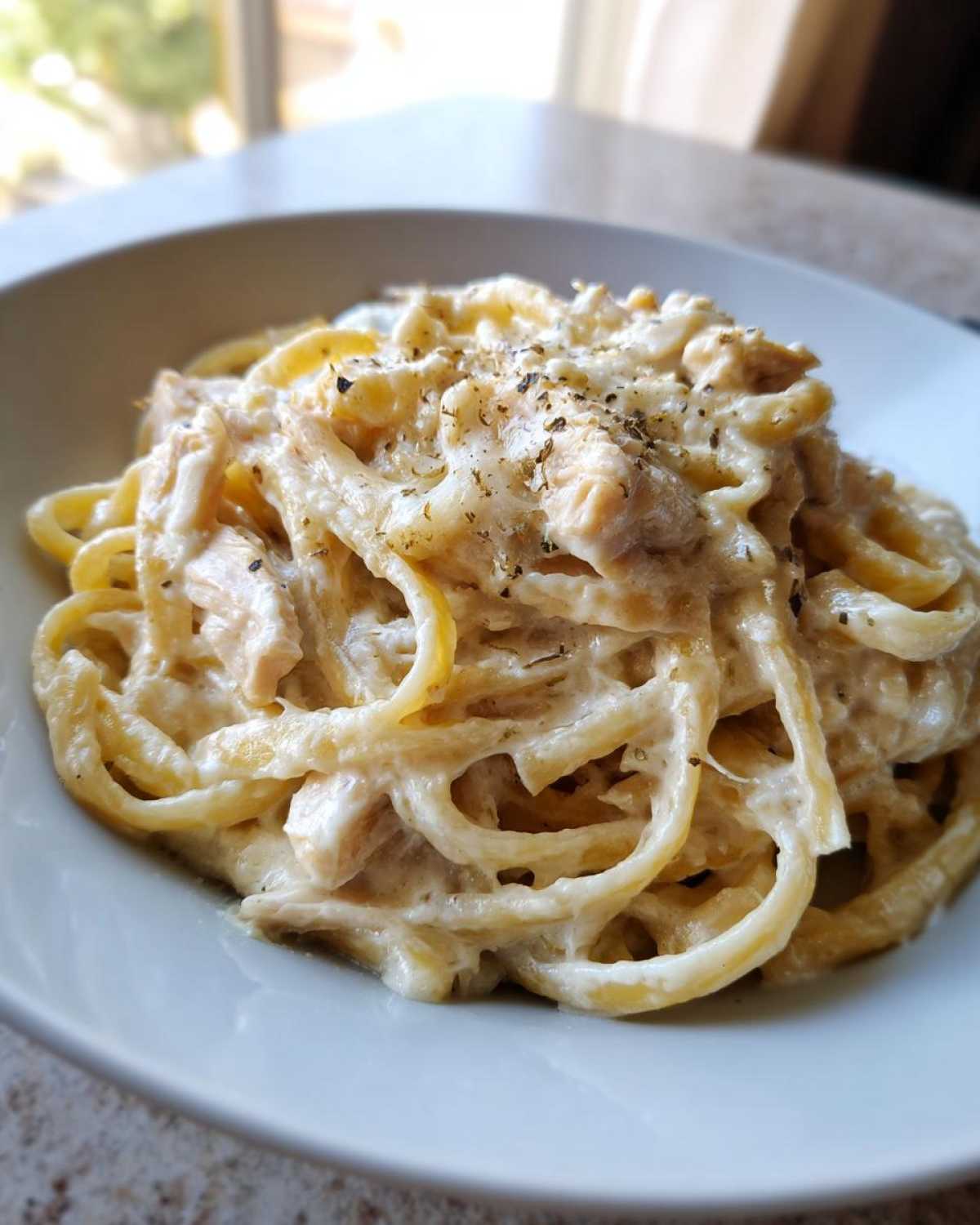 Close-up of a bowl filled with luscious Creamy Alfredo Pasta with Chicken and Cheese, topped with black pepper.