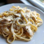 A close-up serving of fettuccine pasta coated in a rich, creamy sauce with shredded chicken, seasoned with black pepper, making up our Creamy Alfredo Pasta with Chicken and Cheese.