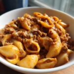 A white bowl filled with creamy beef and shells pasta, featuring ground beef in a rich sauce and melted cheese.