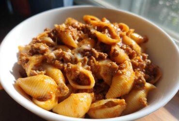 A white bowl filled with creamy beef and shells pasta, featuring ground beef in a rich sauce and melted cheese.