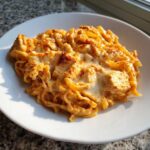 A serving of Creamy Cajun Chicken Alfredo Bake with melted cheese and seasoned chicken chunks on a white plate.