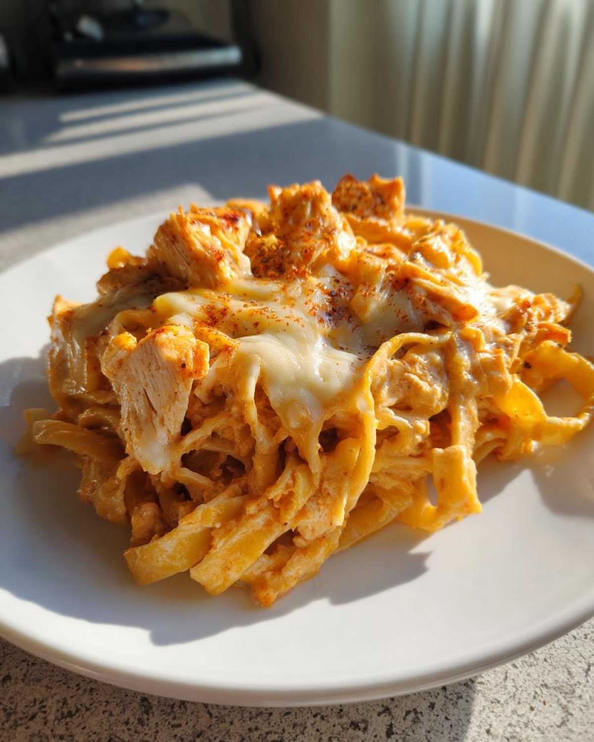 A close-up of a serving of Creamy Cajun Chicken Alfredo Bake with melted cheese and chicken pieces.