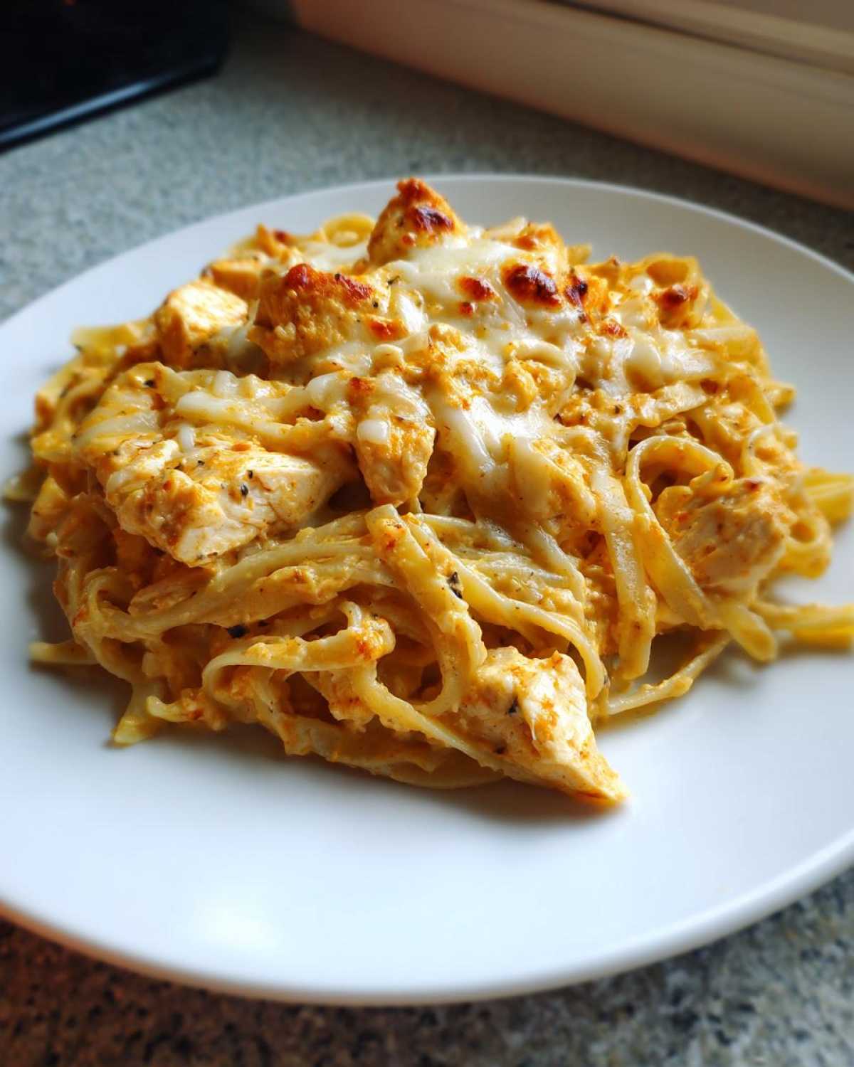 A close-up of a serving of Creamy Cajun Chicken Alfredo Bake with melted, slightly browned cheese on top.