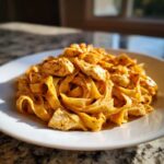 A close-up of Creamy Cajun Chicken Pasta with Bold Flavor featuring fettuccine noodles and seasoned chicken chunks on a white plate.